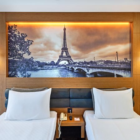 Sealife Family Resort Hotel Antalya Exterior photo The photo depicts a hotel room featuring two single beds with white bedding. Behind the beds, there's a large mural of the Eiffel Tower, set against a scenic backdrop of the Seine River. The image has a vintage, sepia-toned appearance, enhancing the 