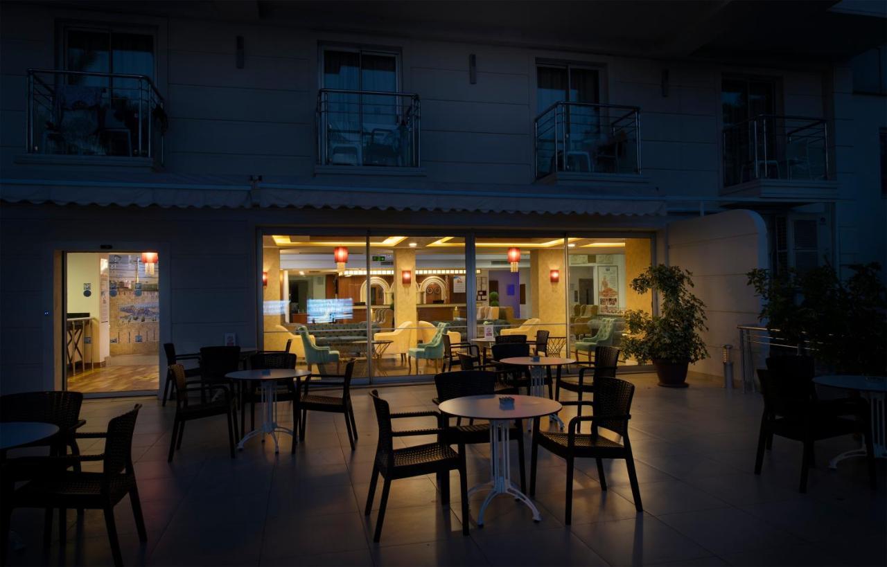 Sealife Family Resort Hotel Antalya Exterior photo The photo depicts an outdoor seating area of a café or restaurant. In the foreground, there are several black chairs and a small round table. In the background, through large windows, you can see the interior of the establishment, which is warmly lit