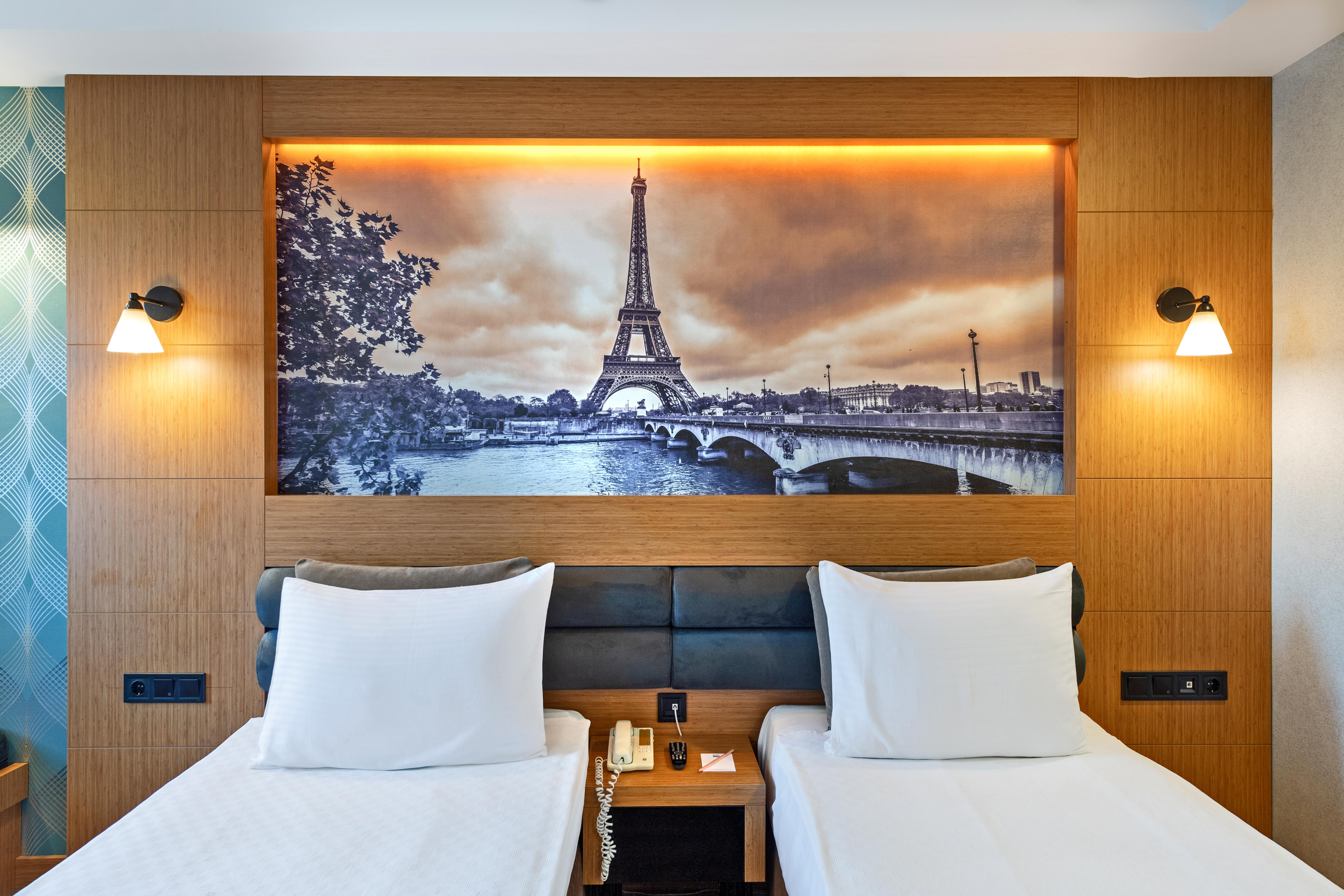 Sealife Family Resort Hotel Antalya Exterior photo The photo depicts a hotel room featuring two single beds with white bedding. Behind the beds, there's a large mural of the Eiffel Tower, set against a scenic backdrop of the Seine River. The image has a vintage, sepia-toned appearance, enhancing the 