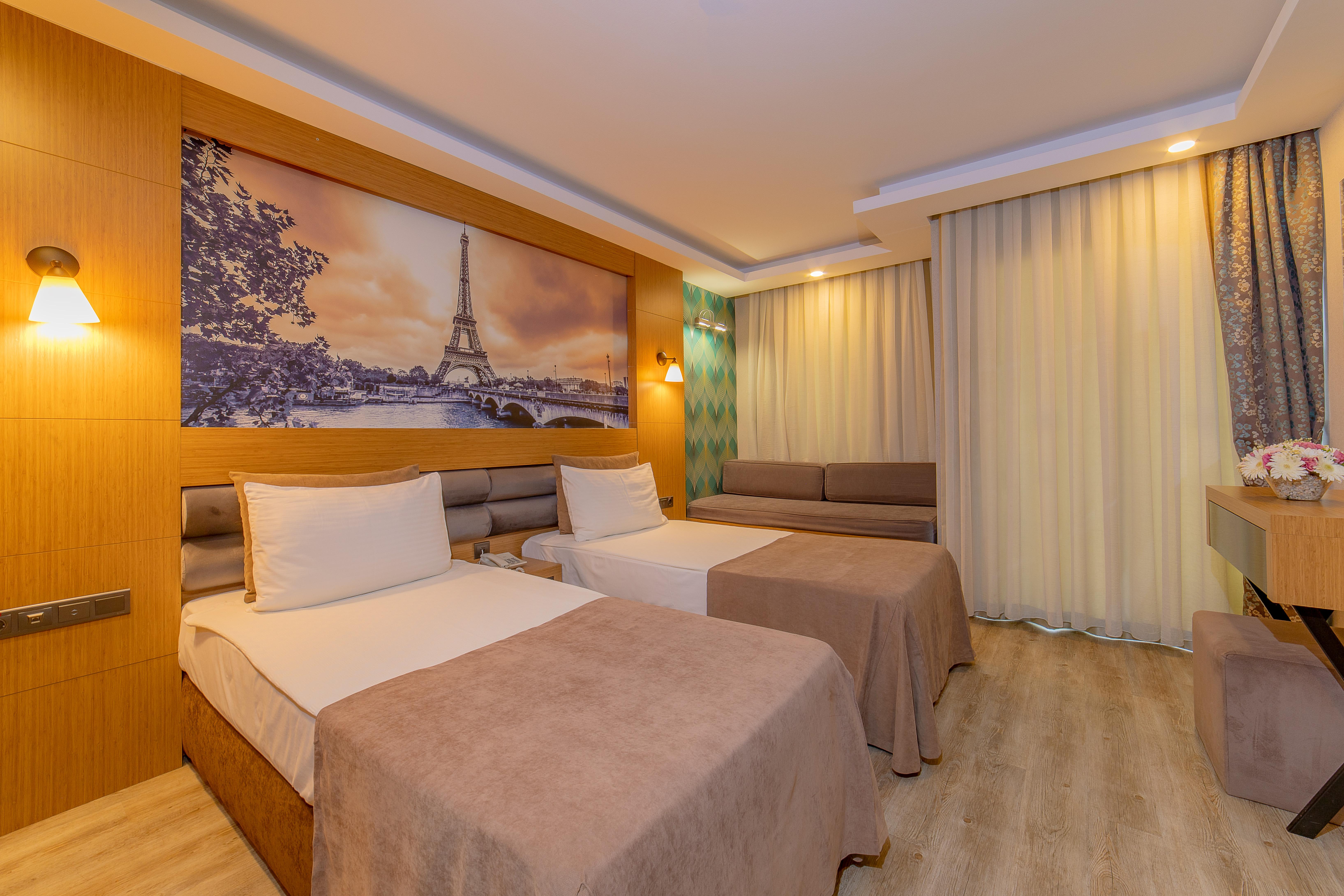 Sealife Family Resort Hotel Antalya Exterior photo The photo shows a modern hotel room featuring two beds with beige bedspreads. There is a large wall mural depicting a scenic view of the Eiffel Tower in Paris. The room is well-lit, with soft lighting fixtures on the walls. To the right, there is a s