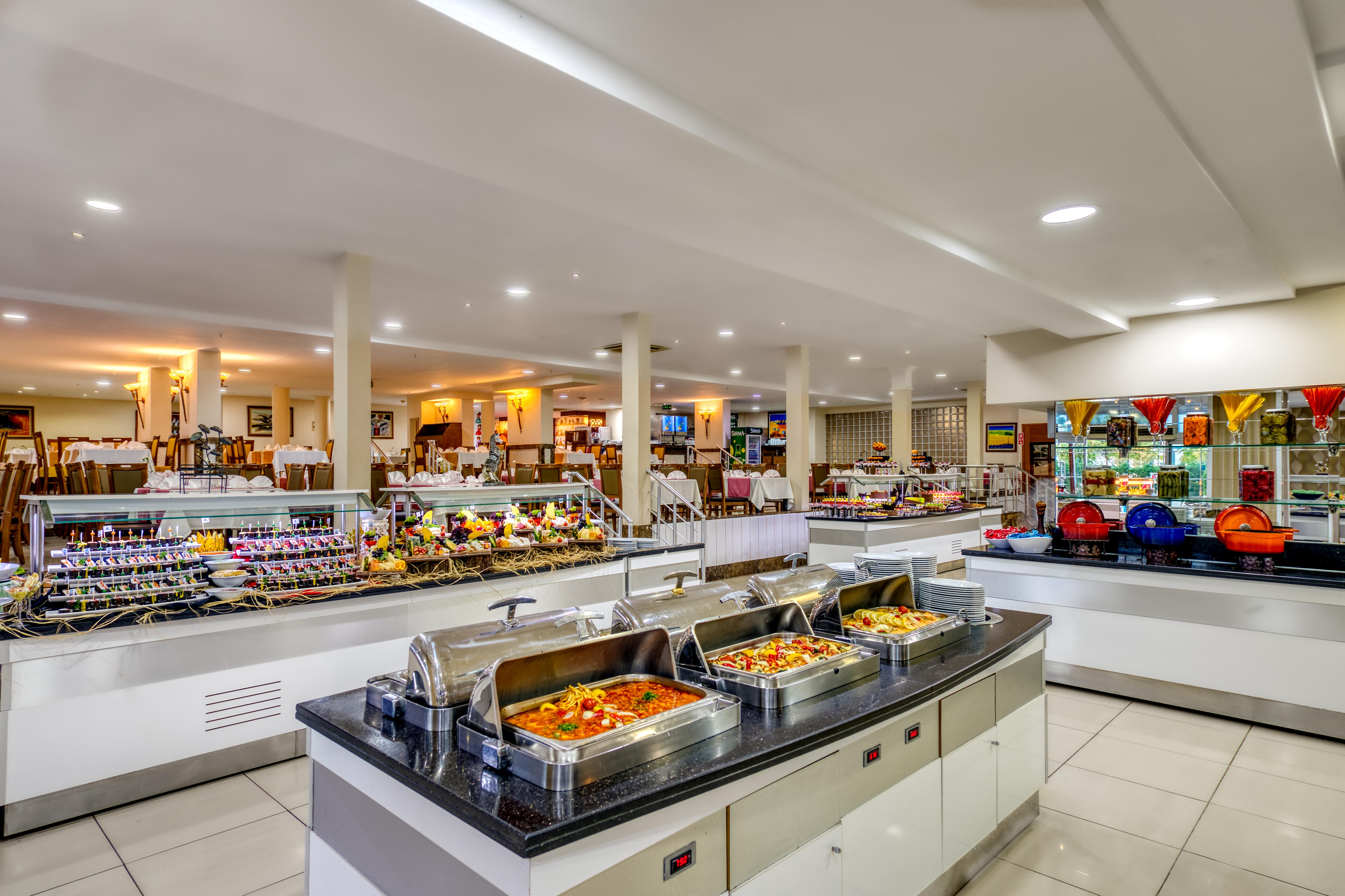 Sealife Family Resort Hotel Antalya Exterior photo The photo shows a spacious buffet area in a restaurant. There are several food stations featuring a variety of dishes. In the foreground, there are chafing dishes that contain warm food, likely offering options like pasta, vegetables, or meats. Behin