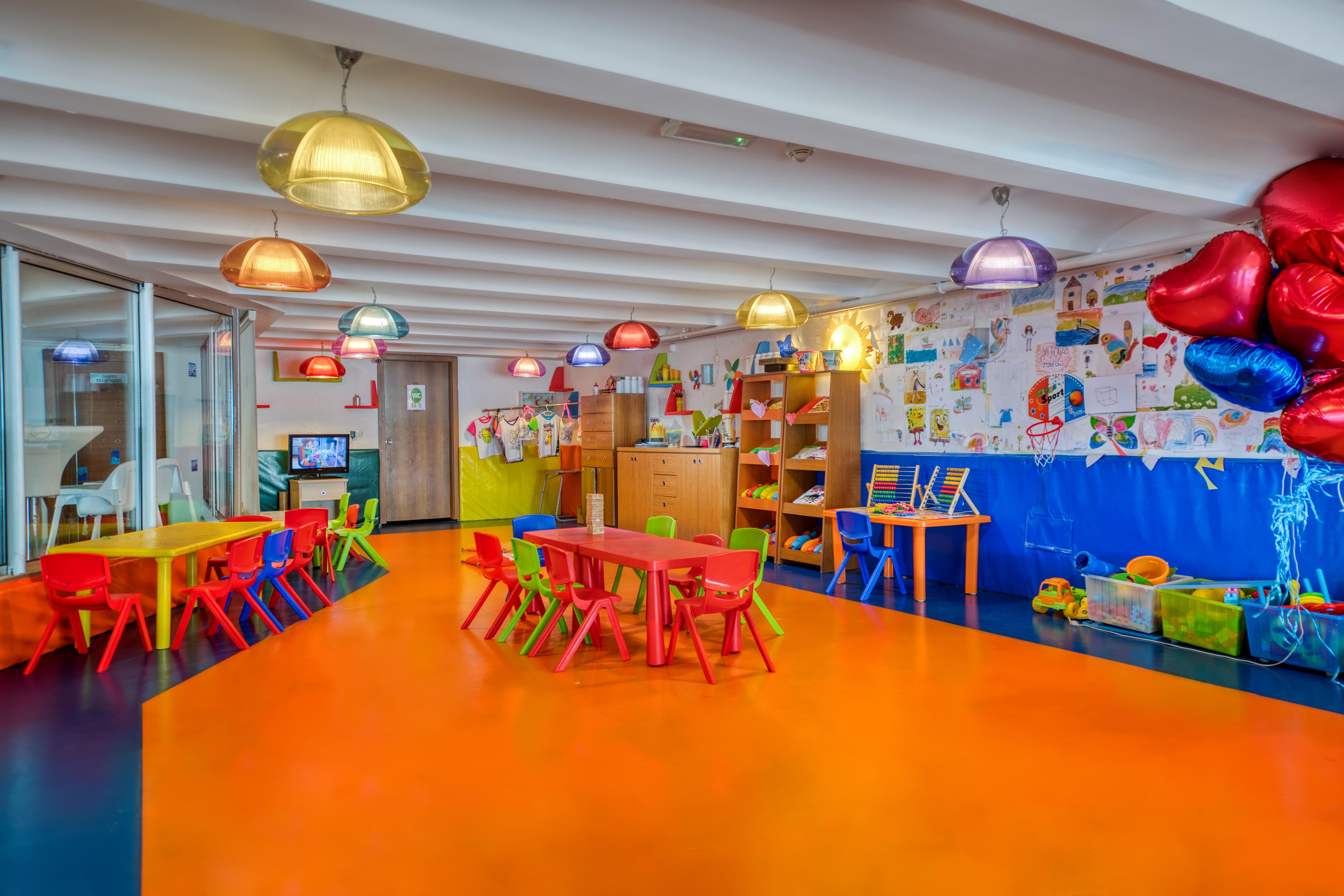 Sealife Family Resort Hotel Antalya Exterior photo The photo shows a vibrant and colorful kindergarten classroom. The flooring is a bright orange, contributing to the cheerful atmosphere. Various tables and chairs are arranged throughout the space, with some in yellow and red. Colorful pendant lights