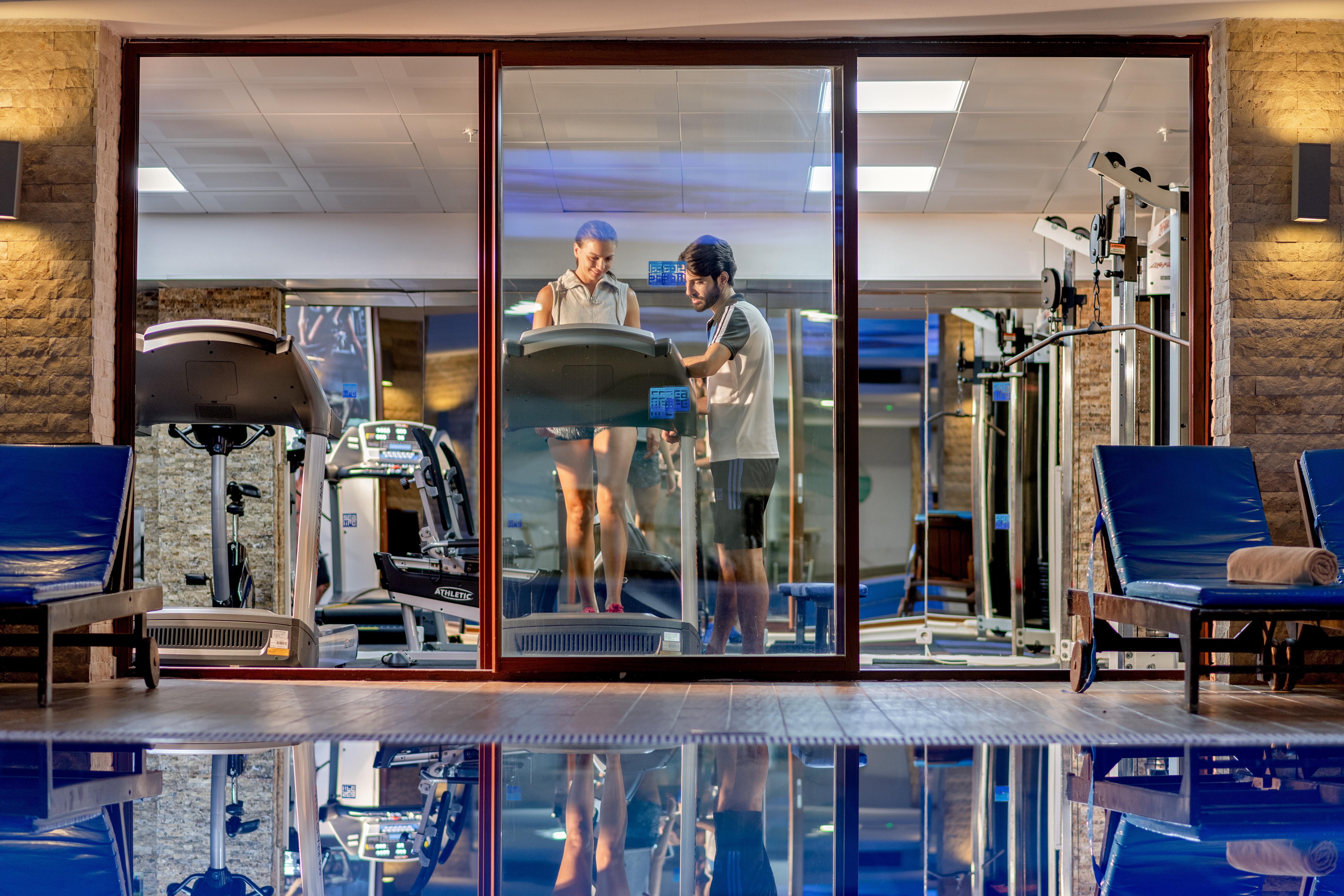 Sealife Family Resort Hotel Antalya Exterior photo The photo shows a modern gym area viewed through a large glass window. Inside the gym, there are two individuals, one on a treadmill and the other standing beside it, possibly offering guidance or support. The gym is well-equipped, featuring various 