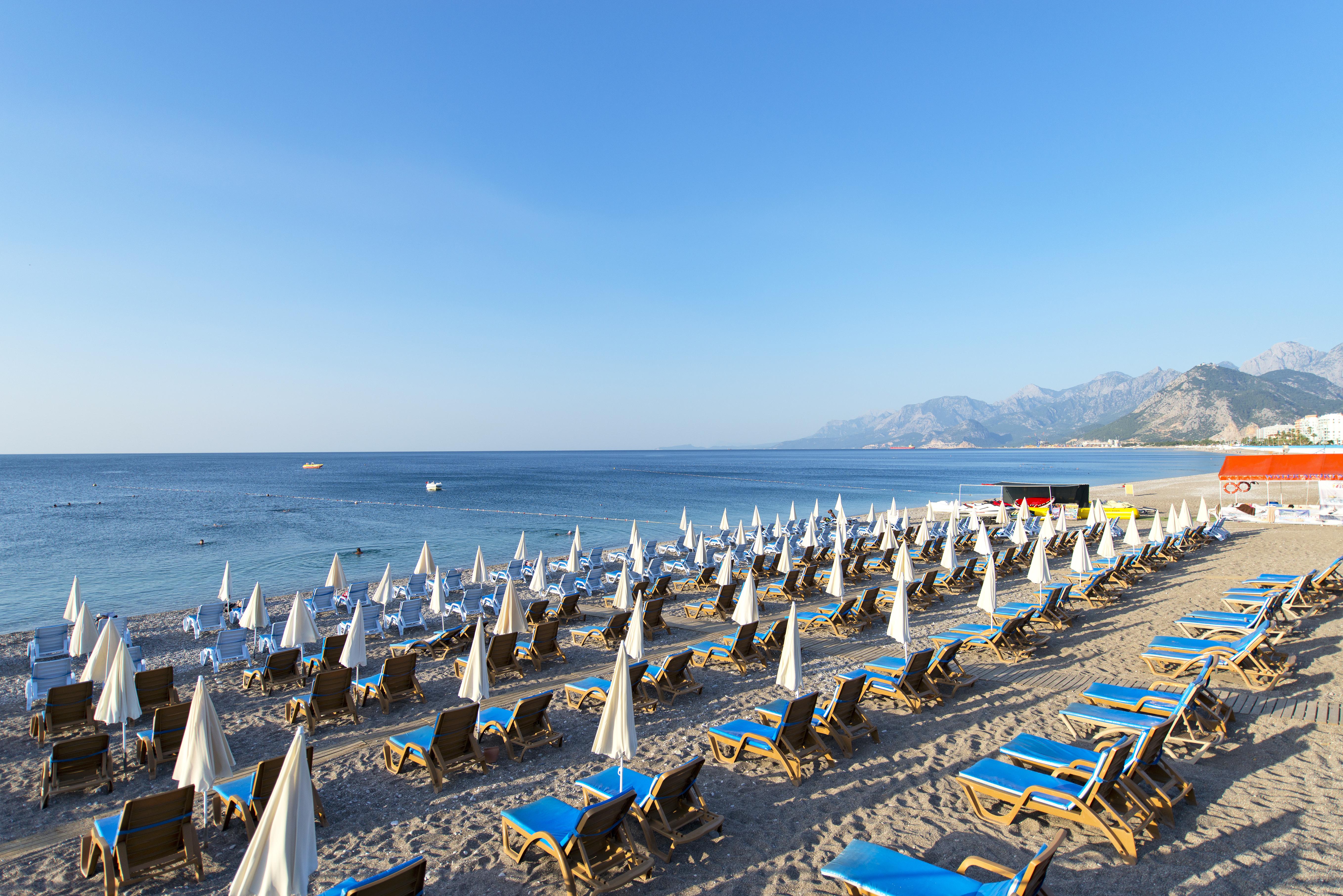 Sealife Family Resort Hotel Antalya Exterior photo The photo depicts a beach scene with numerous sun loungers arranged in rows on the sand, each equipped with white umbrellas. The loungers are primarily blue, creating a vibrant contrast against the sandy beach. In the background, gentle waves can be 