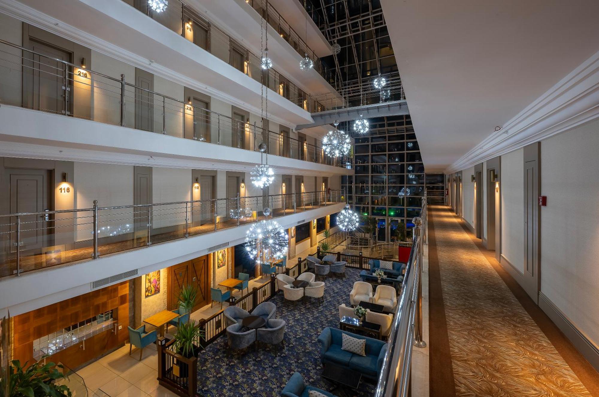 Sealife Family Resort Hotel Antalya Exterior photo The image shows the interior of a hotel lobby or atrium. It features multiple levels with balconies overlooking a central area. The design includes elegant lighting fixtures that resemble decorative spheres, hanging from the ceiling. The floor is ado